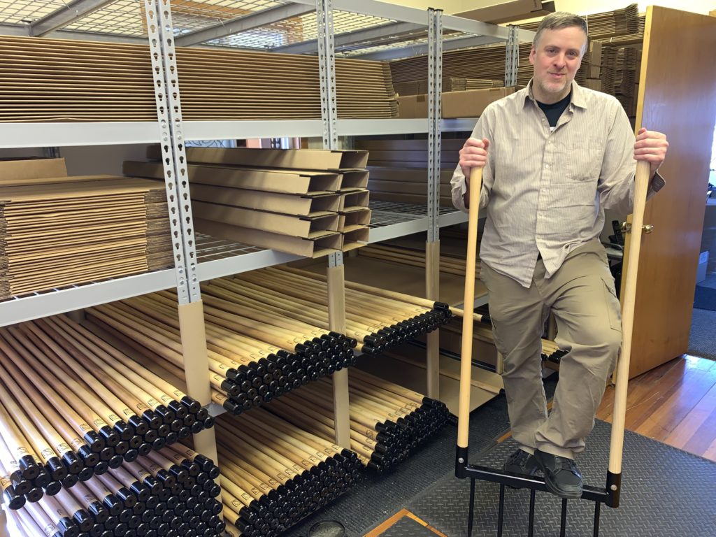 Andy standing with a broadfork in front of storage bays filled with long handles and boxes