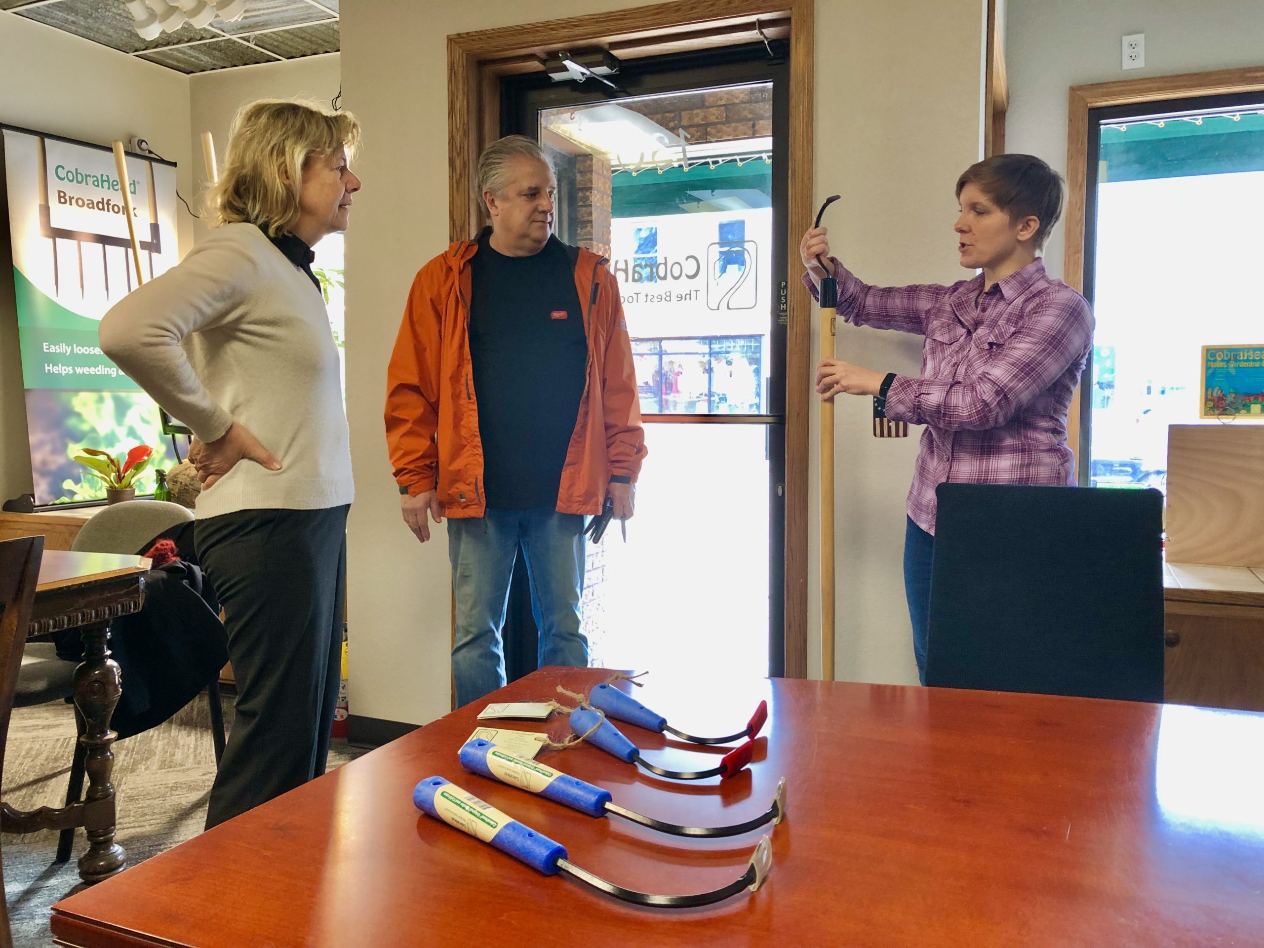Tammy Baldwin and Craig Carpenter look on while Anneliese Valdes holds a CobraHead Long Handle tool